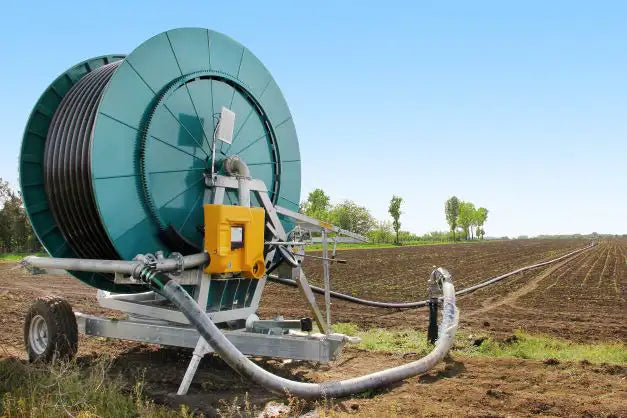 Large irrigation system in a field, featuring a giant green reel with hoses, set against a backdrop of a freshly plowed field under a clear sky, symbolizing modern agricultural technology.