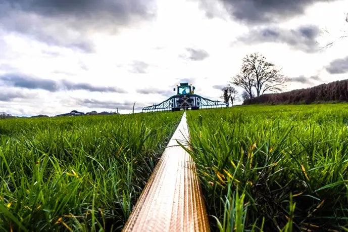 Low angle view of a hose leading through vibrant green grass towards a distant green farm tractor under a cloudy sky, depicting a rural setting with a focus on leading lines in the composition
