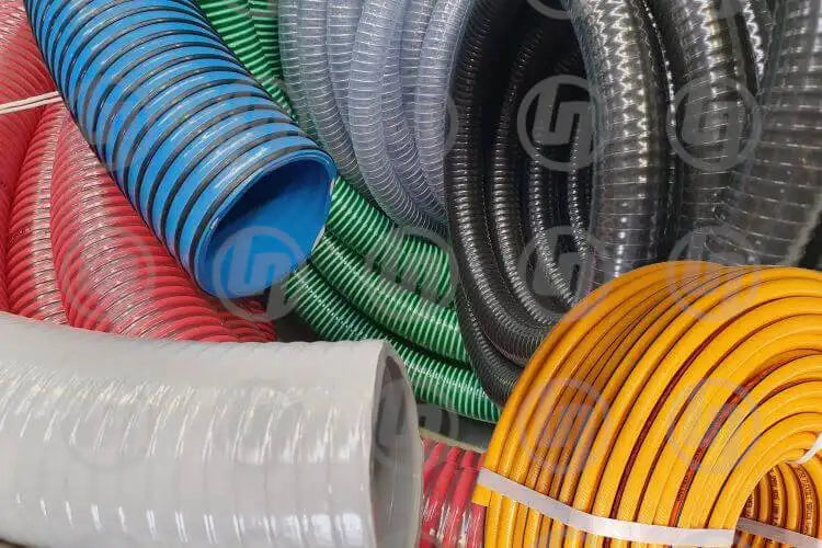 Assortment of colorful industrial hoses and pipes, including blue, green, red, and orange, coiled and stacked in a display, showcasing various types and sizes used for different engineering purposes.