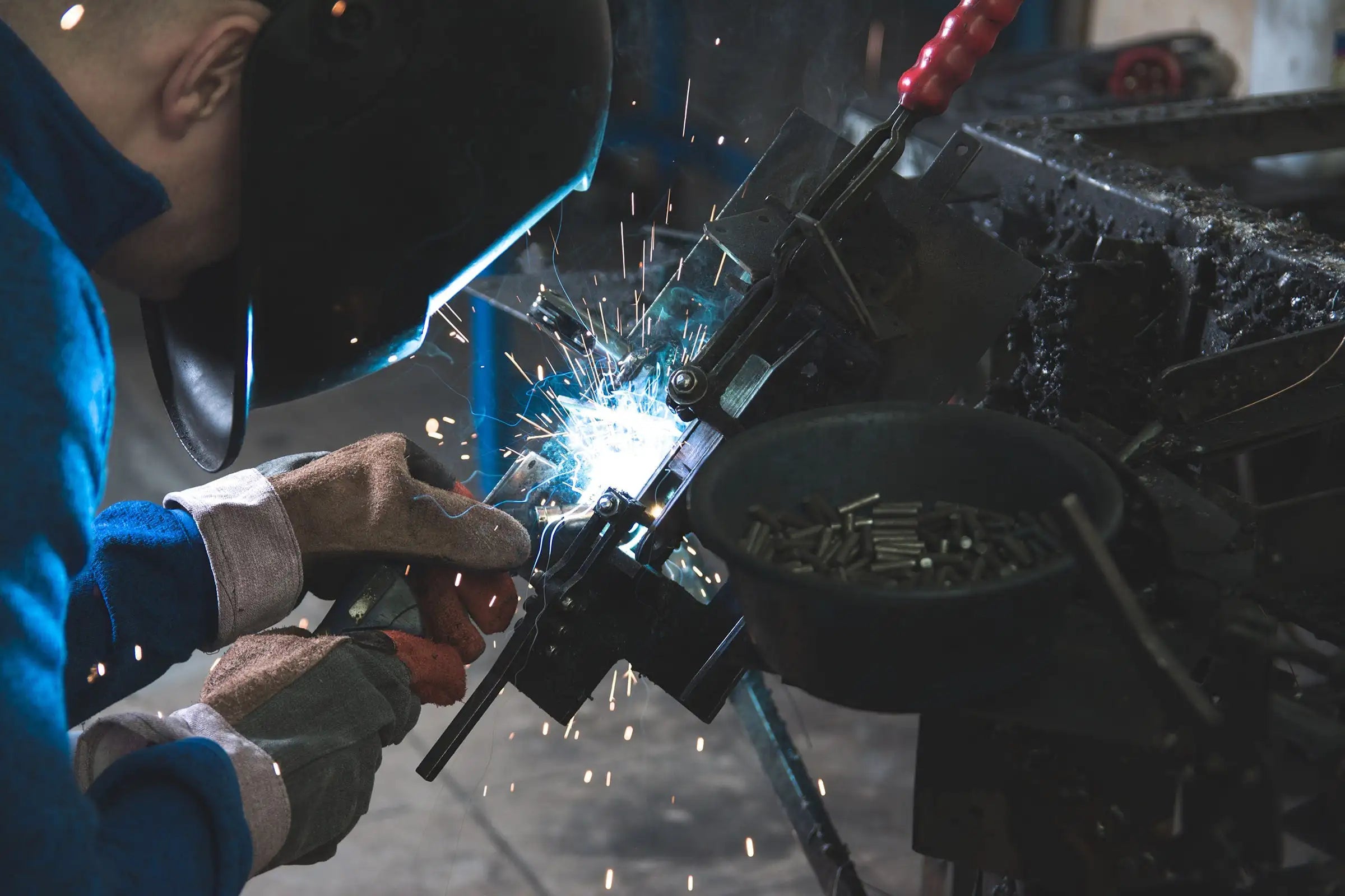 Close-up of a skilled worker welding metal parts in an industrial setting, with sparks flying around as he concentrates on his task, wearing protective gear including a helmet and gloves.