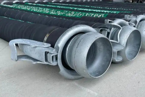 Close-up view of large industrial hoses with metal couplings stacked on a concrete floor, highlighting the texture and robust construction of the equipment used in industrial applications.