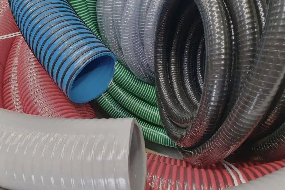 Assortment of colorful industrial hoses and pipes, including blue, green, red, and grey, coiled and stacked in a display, showcasing various types and sizes used for different engineering purposes.
